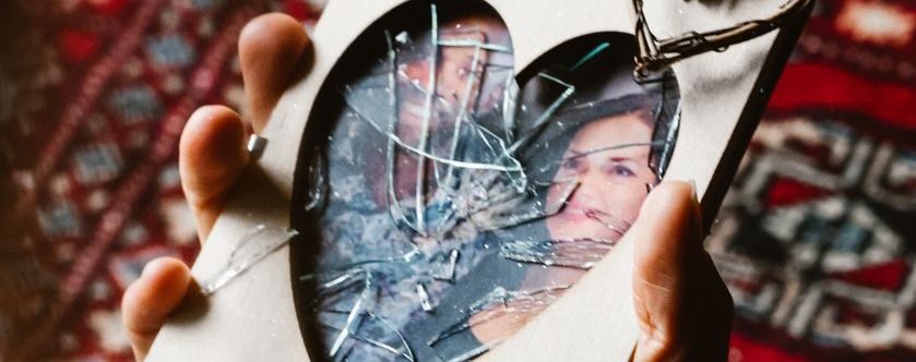 A close-up of a hand holding a broken heart-shaped picture frame on a patterned rug.