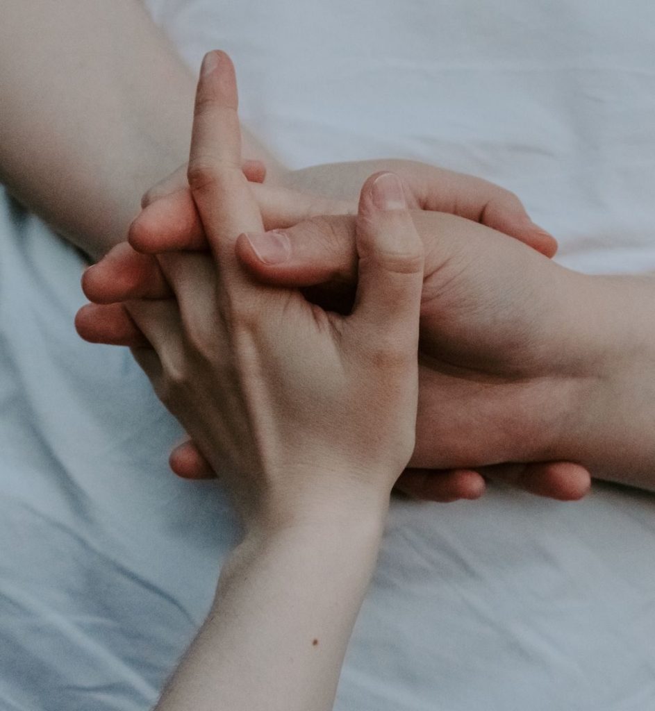 Intimate close-up of hands interlocked on a soft surface, symbolizing connection and love.